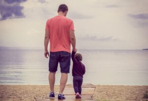 a father and a son holding hands and looking at a river